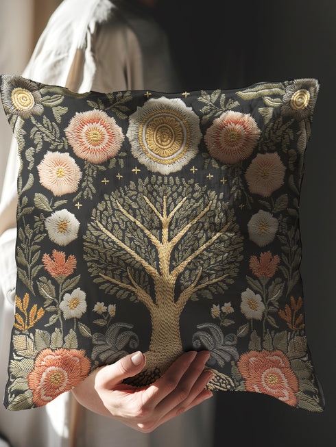 A square charcoal black decorative pillow cover made from a linen-feel fabric. The design features a large, central Tree of Life in antique gold and sage green, with intricate roots at the base. The tree is surrounded by a symmetrical pattern of stylized folk art flowers in muted blush pink, terracotta, and off-white. The print has a faux embroidered, tapestry-style texture. In each of the four corners is a circular, sun-like medallion, completing the ornate, botanical noir design.